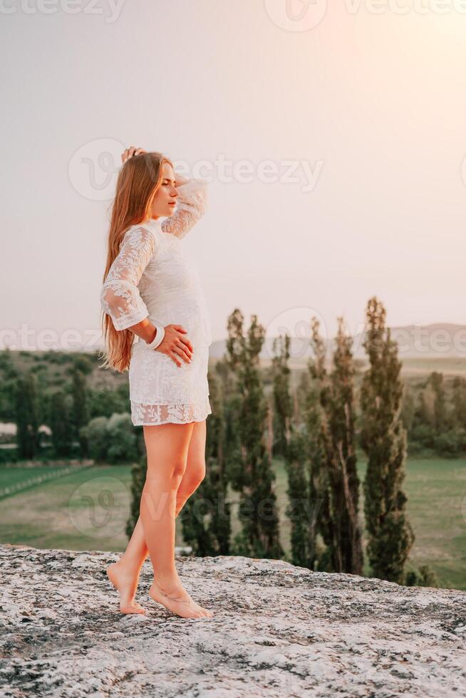 glücklich Frau im Weiß Boho Kleid auf Sonnenuntergang im Berge. romantisch Frau mit lange Haar Stehen mit ihr zurück auf das Sonnenuntergang im Natur im Sommer- mit öffnen Hände. Silhouette. Natur. Sonnenuntergang. foto