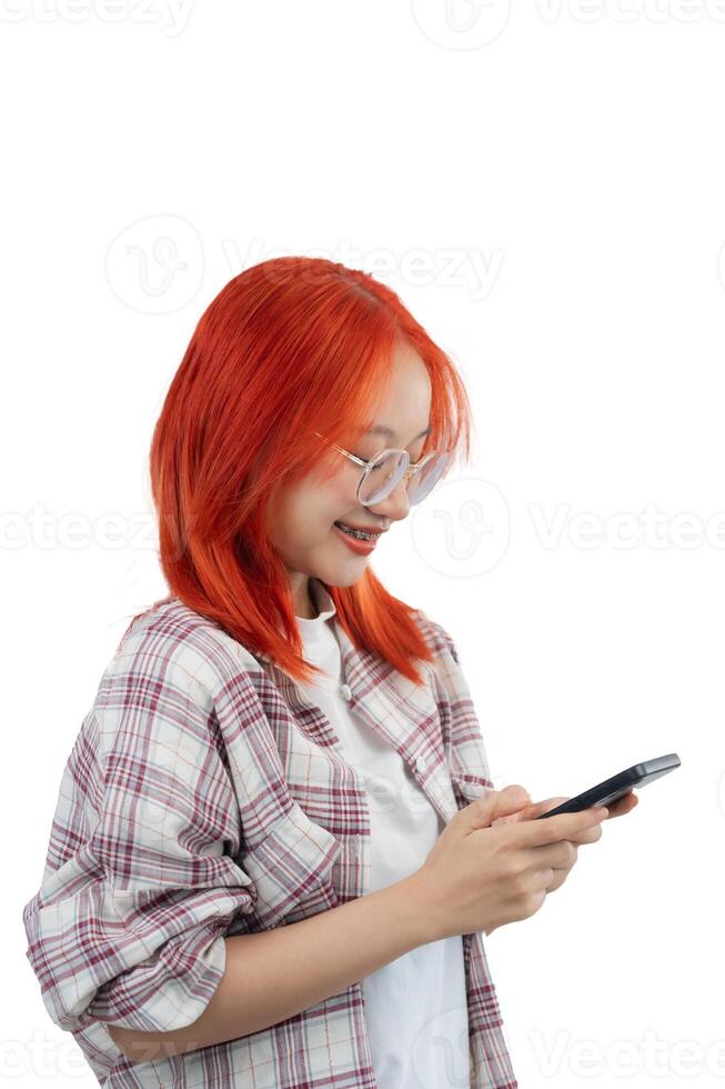 ein Frau mit rot Haar und Brille ist suchen beim ihr Zelle Telefon. sie ist lächelnd und sie ist genießen Sie selber. isoliert auf Weiß Hintergrund foto