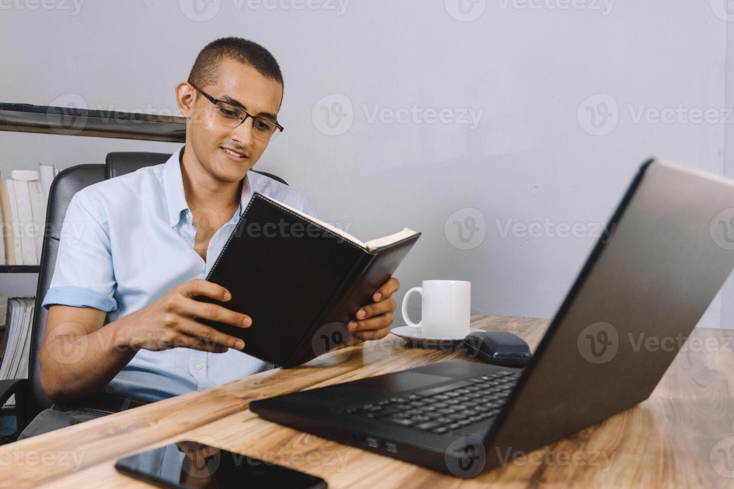 Porträt von ein jung latinx Mann lesen ein Buch. spanisch männlich Schüler Überprüfung seine Anmerkungen auf seine Schreibtisch. foto