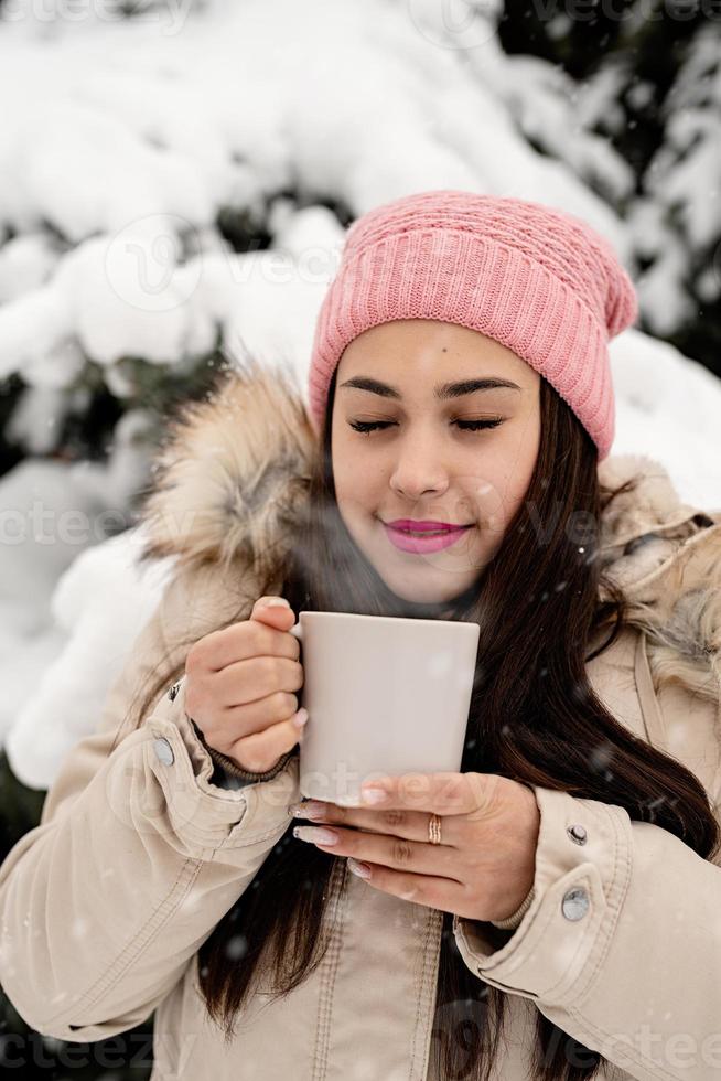 Schöne Frau in warmer Winterkleidung, die an einem verschneiten Tag eine Tasse im Freien trinkt, die heißen Tee oder Kaffee trinkt foto