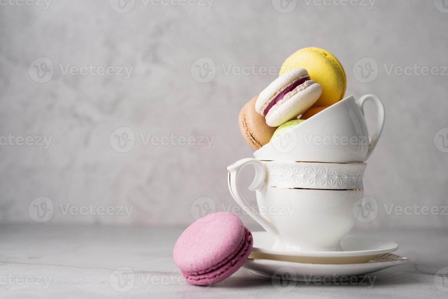 Stapel weiße Kaffeetassen gefüllt mit Makronen am Rand des Tisches, weißer Backsteinmauerhintergrund foto