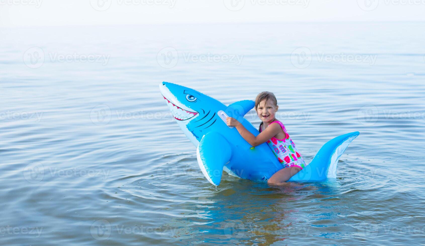 glücklich Mädchen von europäisch Aussehen Alter von 7 Schwimmen auf ein aufblasbar groß Hai Spielzeug im das Meer.Familie Sommer- Berufung Konzept. Kopieren Raum. foto