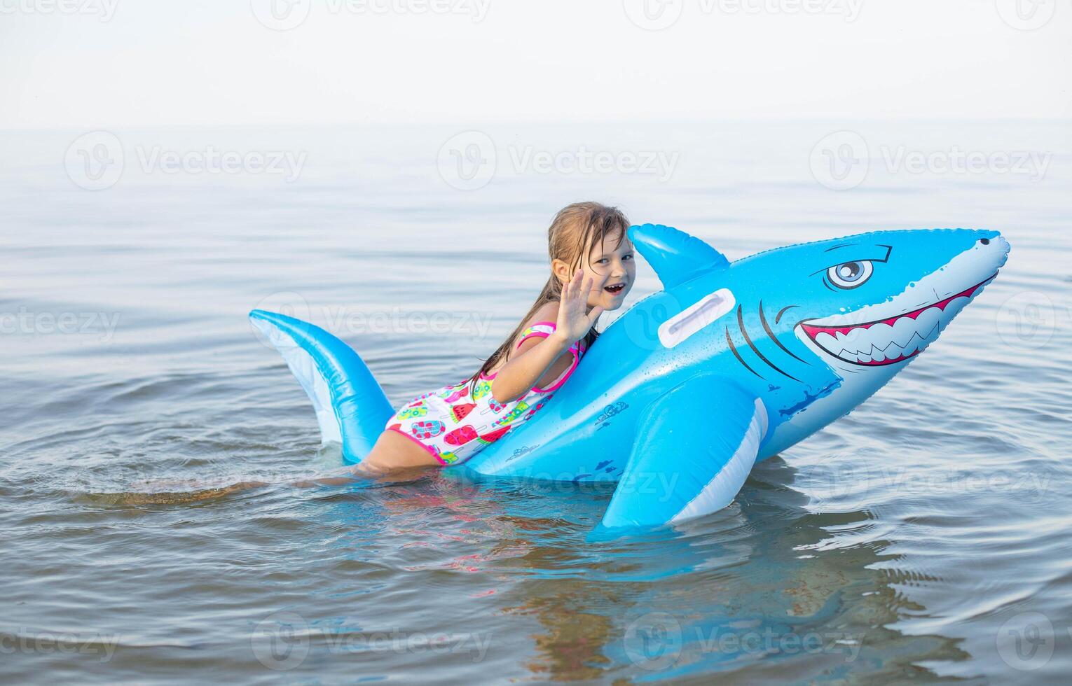 glücklich Mädchen von europäisch Aussehen Alter von 7 Schwimmen auf ein aufblasbar groß Hai Spielzeug im das Meer.Familie Sommer- Berufung Konzept. foto