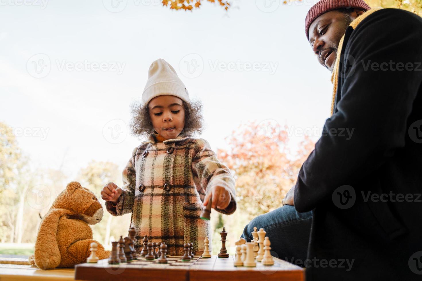 schwarzer Großvater und Enkelin spielen Schach im Herbstpark foto