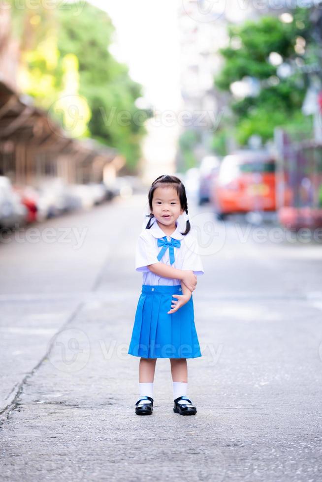 Porträt von asiatischen Schülern Mädchen in blau-weißer Schuluniform. Kind Mädchen wird ein wenig verlegen, wenn Ihre Eltern ein Foto machen, wenn das Baby zum ersten Mal in die Schule geht. süßes lächelndes Kind im Alter von 3 Jahren.