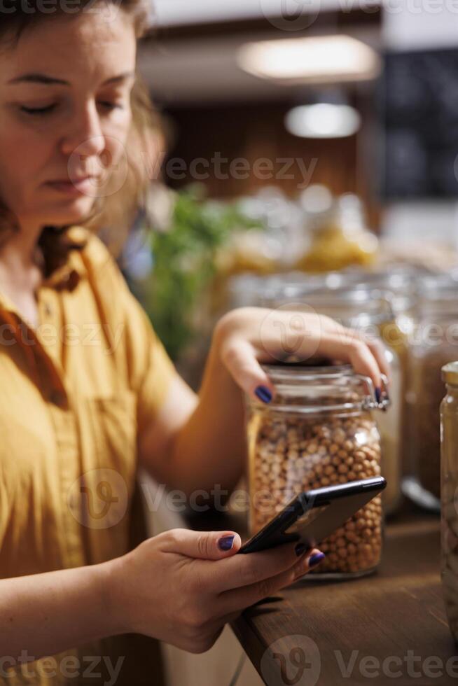 vegan Frau auf ein Diät mit Telefon zu machen sicher Null Abfall Supermarkt Essen ist gut zum ihr Gesundheit. Klient im lokal Gegend Lebensmittelgeschäft Geschäft Herstellung sicher Produkte sind natürlich foto