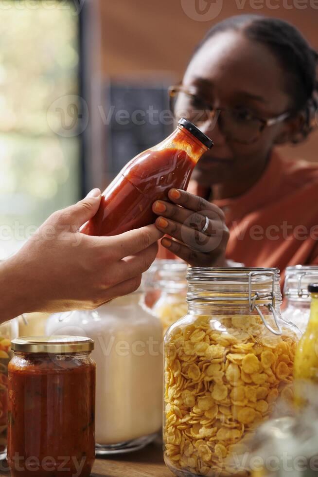 Kunde Einkaufen zum vegan nachhaltig Essen Artikel im ein Null Abfall Geschäft mit Verkäufer Bereitstellung Information. ökologisch freundlich Frau Analysieren hausgemacht Saucen Ideal zum gesund Essen. foto