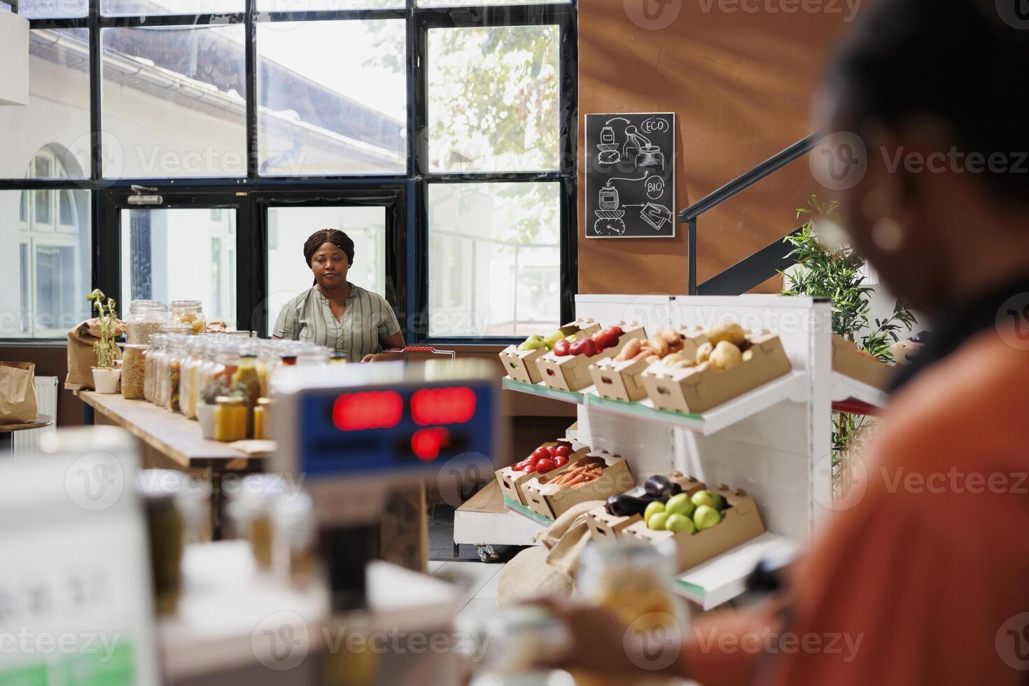 schwarz Frau durchsucht Supermarkt, Fokussierung auf organisch, Öko freundlich Produkte. weiblich Klient halten Korb bereit zu Kauf frisch, gesund Essen beim nachhaltig lokal Lebensmittelgeschäft speichern. foto