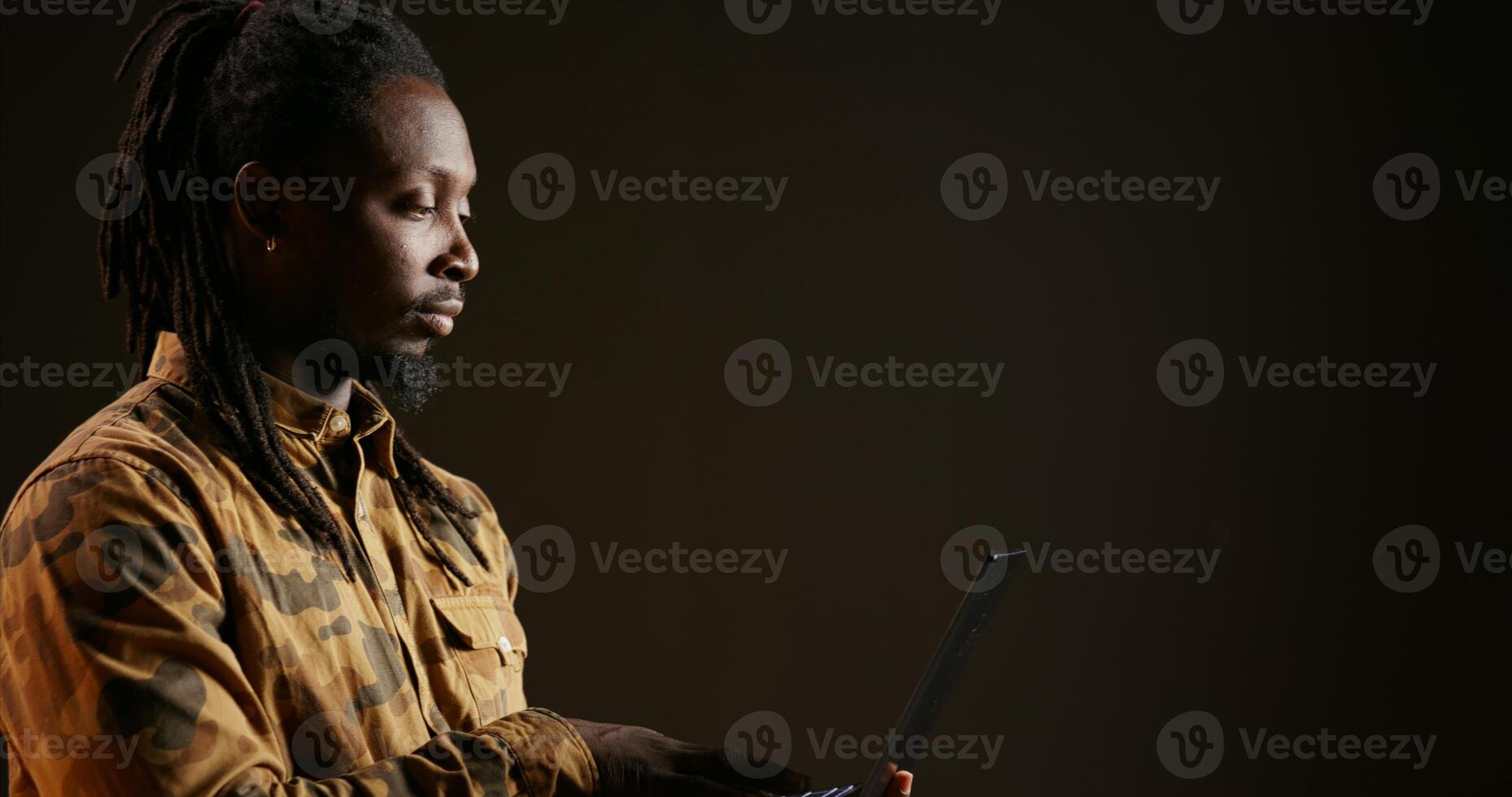 afrikanisch amerikanisch Kerl Scrollen durch online Netzwerk Seiten, suchen zum etwas während er Verwendet Laptop Über schwarz Hintergrund. jung Erwachsene halten kabellos pc und suchen das Webseiten. foto