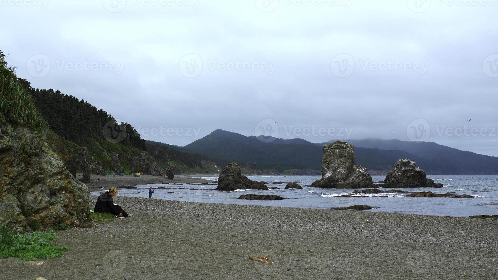 Menschen entspannen auf felsig Küste mit Berge auf wolkig Tag. Clip. schön Küste mit Felsen und Felsen kleben aus auf Ufer. Menschen entspannen auf schön Küste mit Felsen und Berge foto