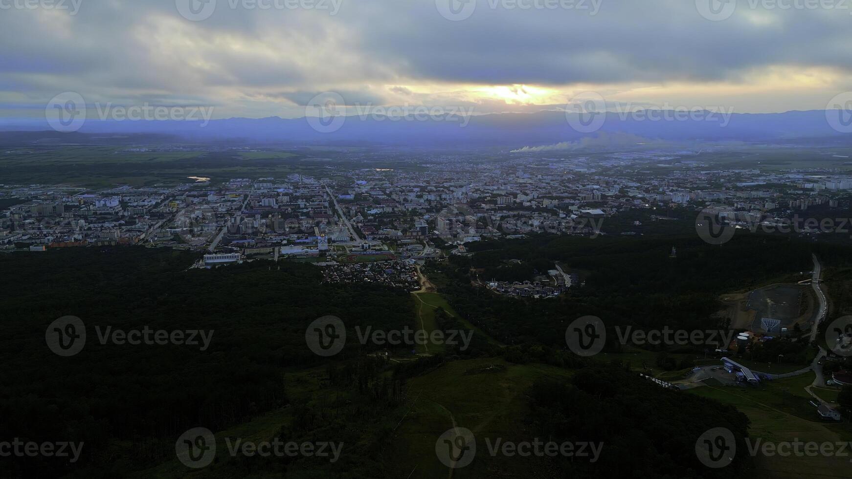 Antenne von das Stadt und groß Grün Hügel. Clip. Sommer- groß Stadt und wolkig Himmel während Sonnenuntergang. foto