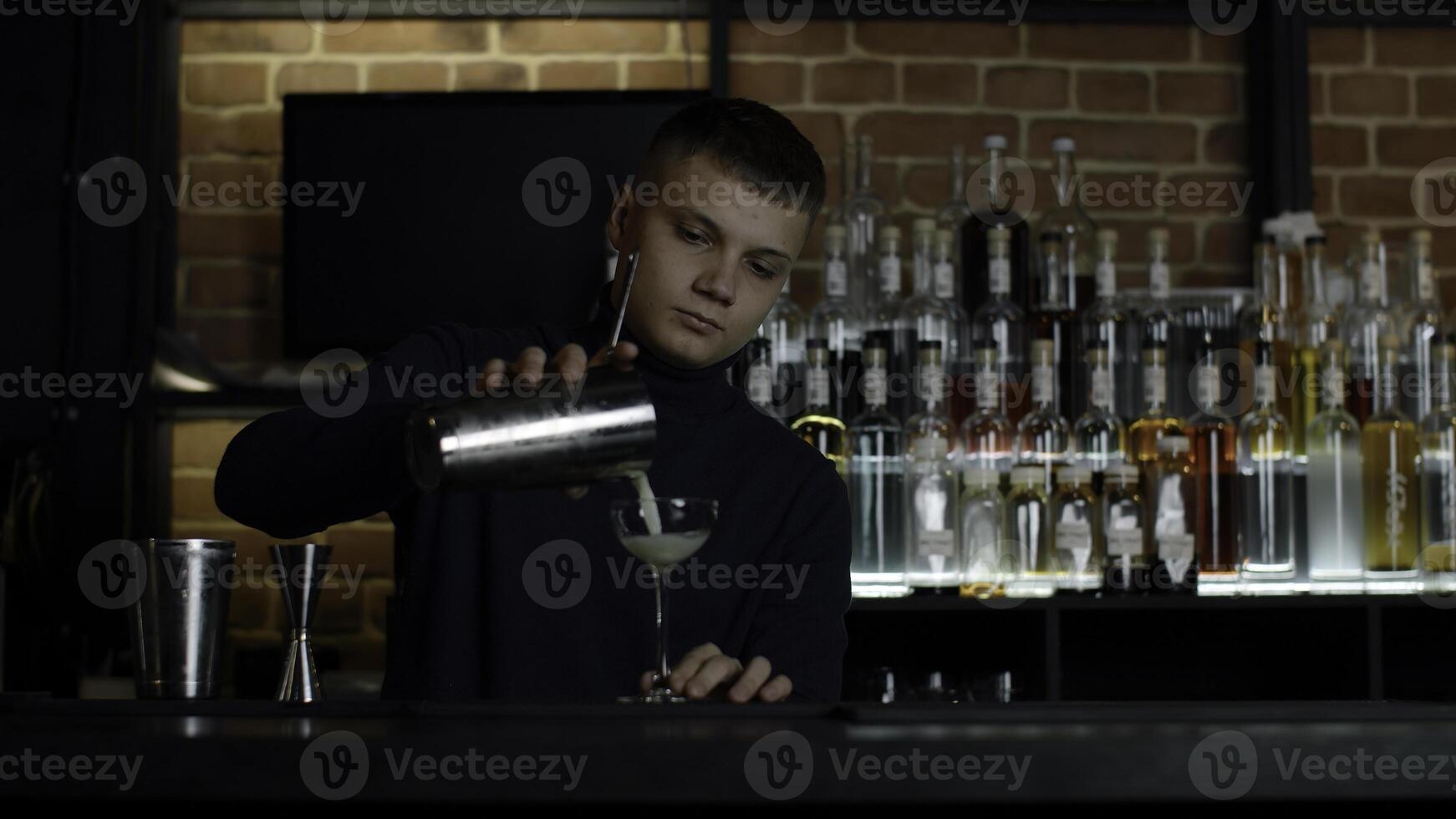 das Barmann vorbereiten perfekt Cocktail, Stehen hinter das Bar Schalter. Medien. viele Flaschen von Alkohol auf das Hintergrund. foto