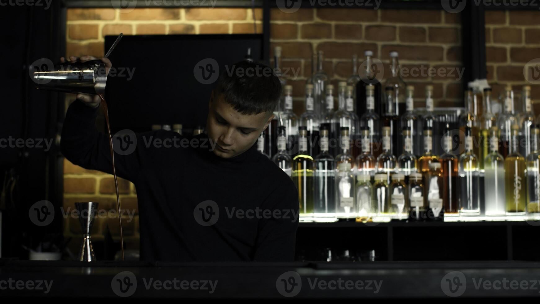 das Barmann vorbereiten perfekt Cocktail, Stehen hinter das Bar Schalter. Medien. viele Flaschen von Alkohol auf das Hintergrund. foto