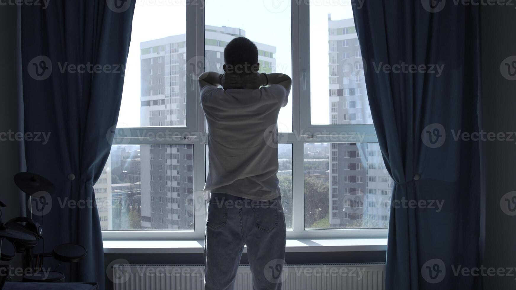 früh Morgen, Silhouette von Mann trainieren, Dehnen Körper durch Fenster beim heim. Medien. Rückseite Aussicht von ein jung Mann Stehen gegen Fenster. foto