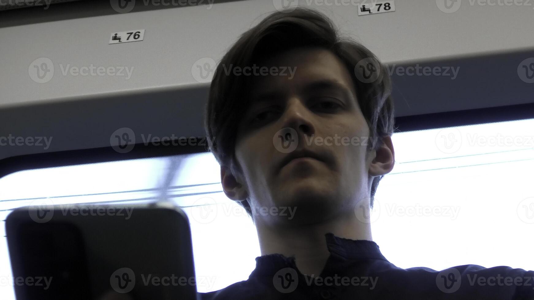 kaukasisch Mann suchen Nieder auf Telefon und suchen betont. Lager Clip. Gesicht von ein Mann Sitzung in der Nähe von das Fenster im das Straßenbahn oder Bus. foto