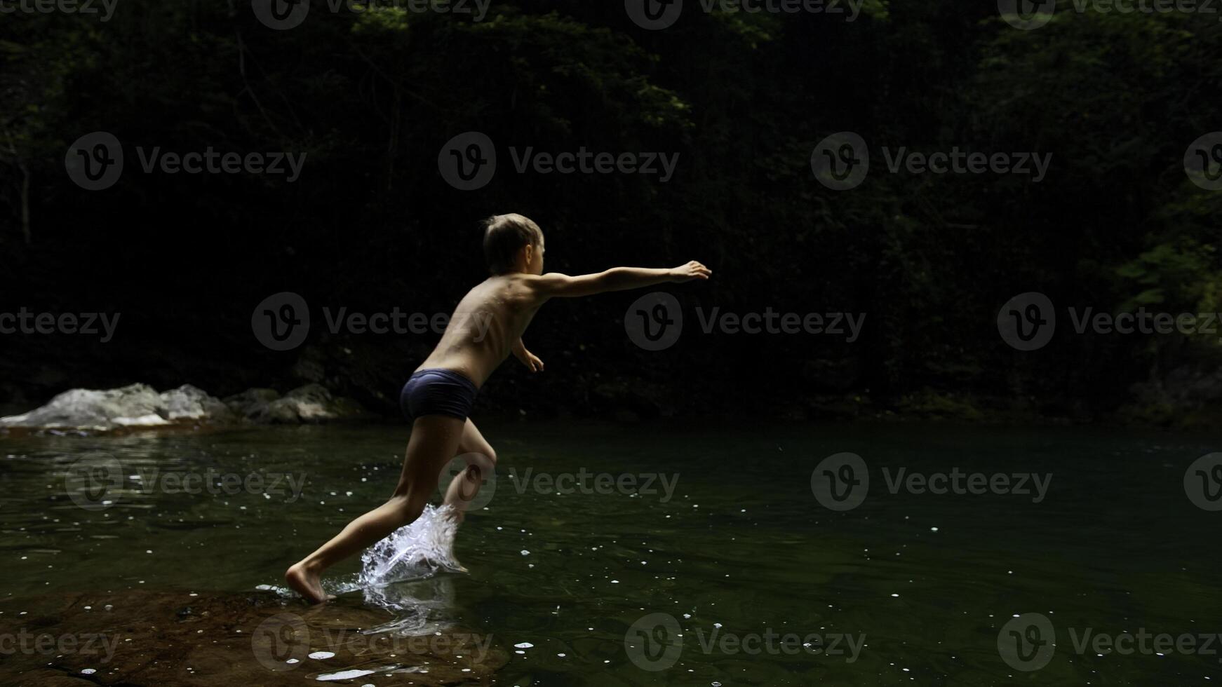 Junge Kind Springen im kalt Berg Fluss auf ein Sommer- Tag. kreativ. Wandern im Sommer- Dschungel. foto