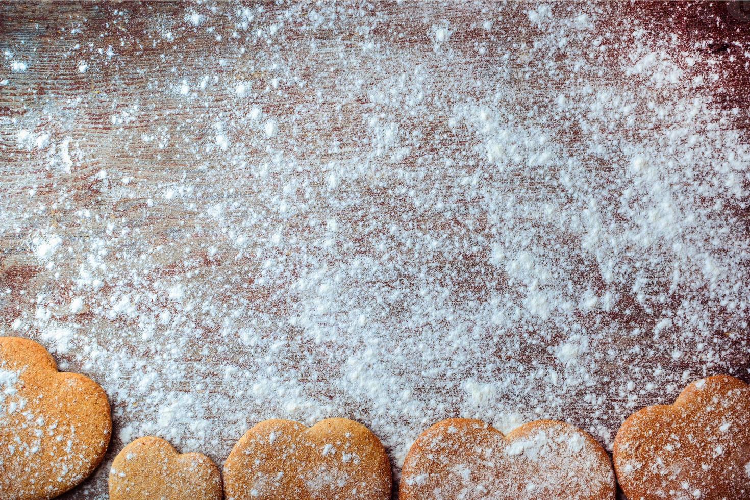 Ingwerplätzchen in Form von Herzen auf einem mit Mehl bestreuten Holztisch. foto