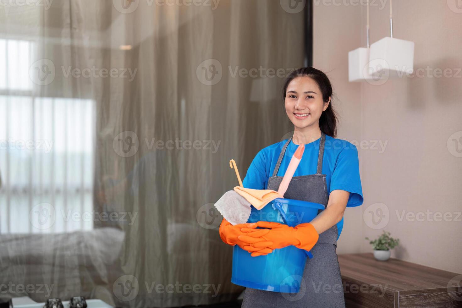 Reinigung Produkt, und Korb mit Frau asiatisch Mitarbeiter Reinigung Bedienung im Schlafzimmer zu sauber Bakterien beim Wohnung. Reiniger oder Maid mit Container zu Arbeit im Zimmer foto