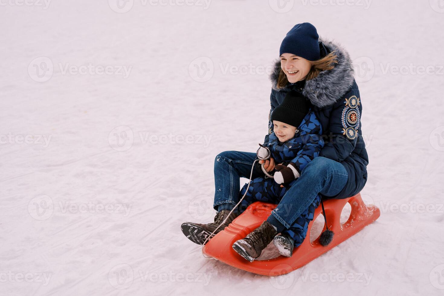 Lachen Mutter mit ein wenig Junge Fahrten ein Schlitten Nieder das Berg foto