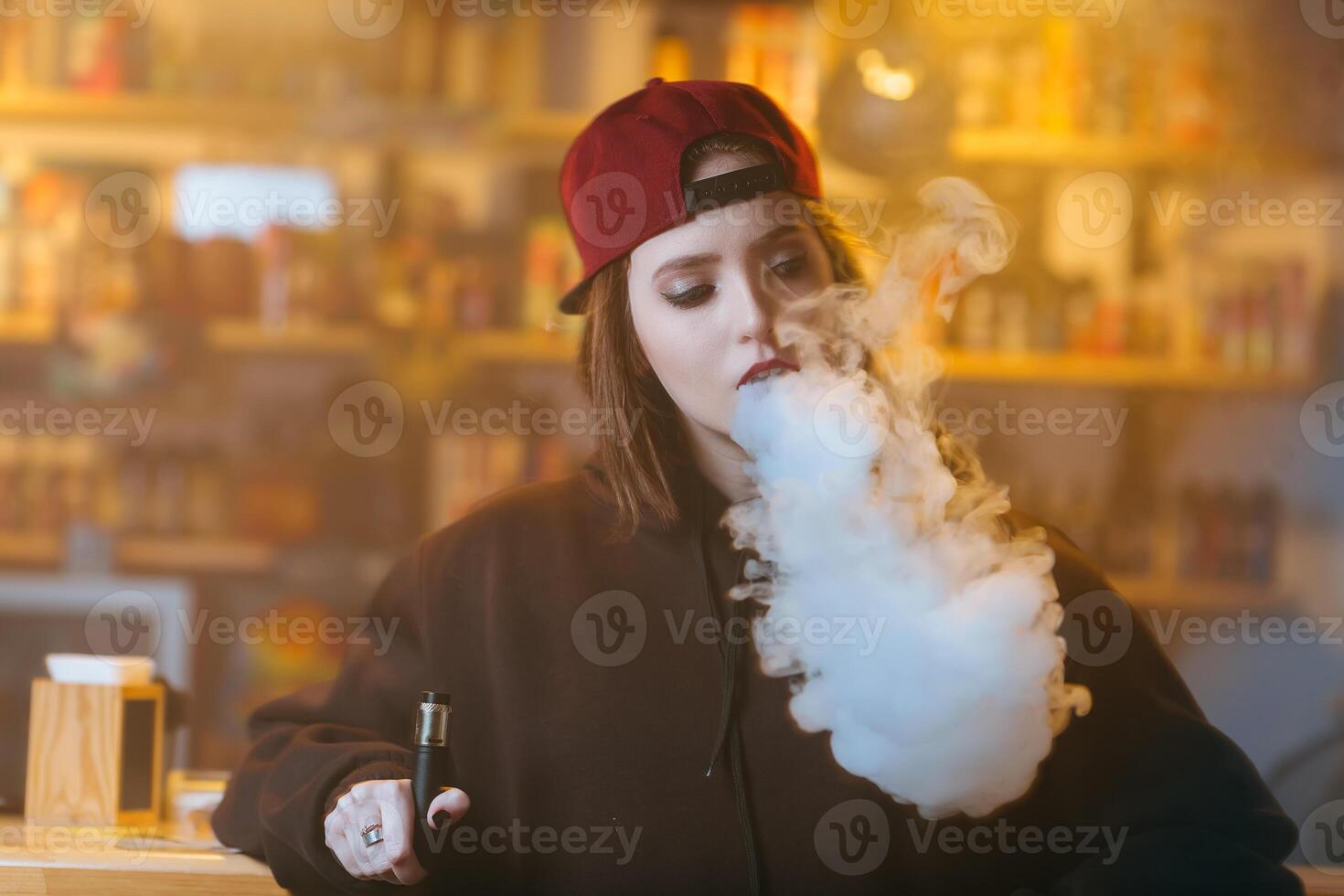 jung ziemlich Frau im rot Deckel Rauch ein elektronisch Zigarette beim das Dampfen Geschäft. HipHop Stil. Nahaufnahme. foto