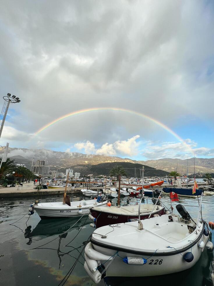 budva, Montenegro - - 25 Dezember 2022. Regenbogen im das Himmel Über das Berge über das Hafen mit festgemacht Yachten foto