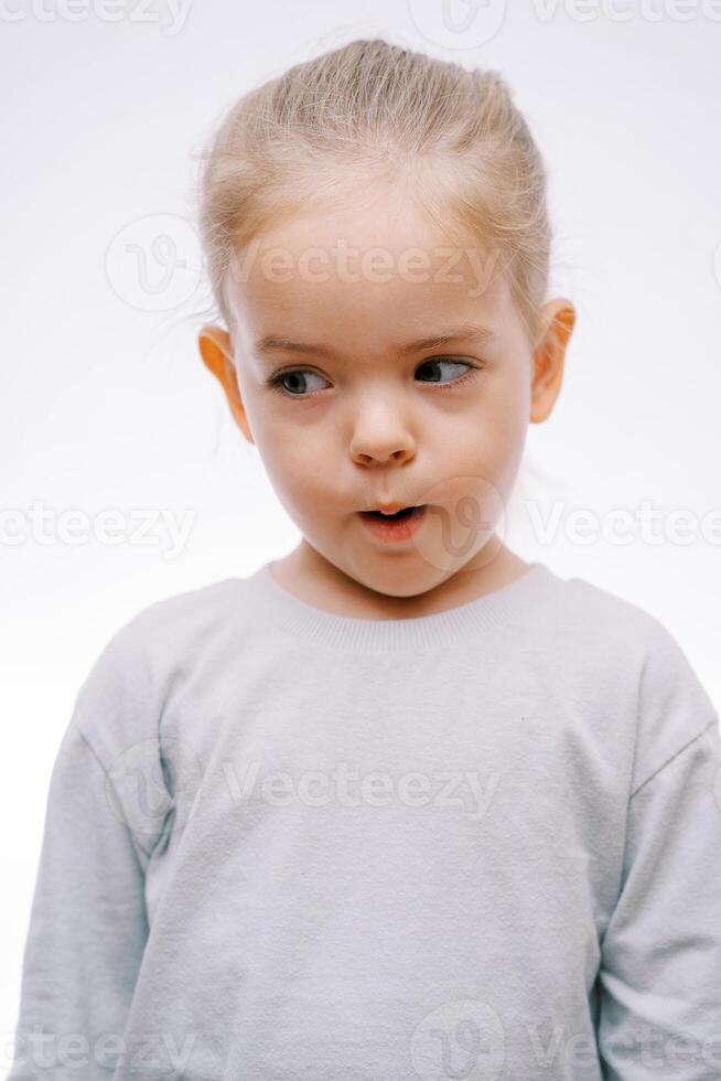 Porträt von ein wenig überrascht Mädchen mit ihr Mund öffnen suchen zu das Seite auf ein grau Hintergrund foto