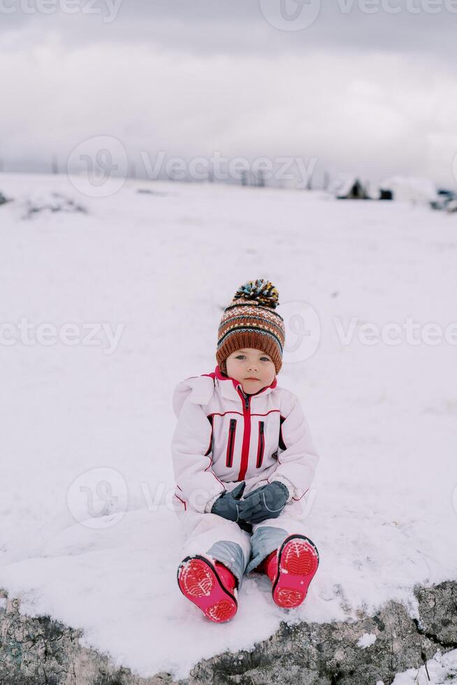 wenig Mädchen Sitzung auf ein schneebedeckt Weide foto