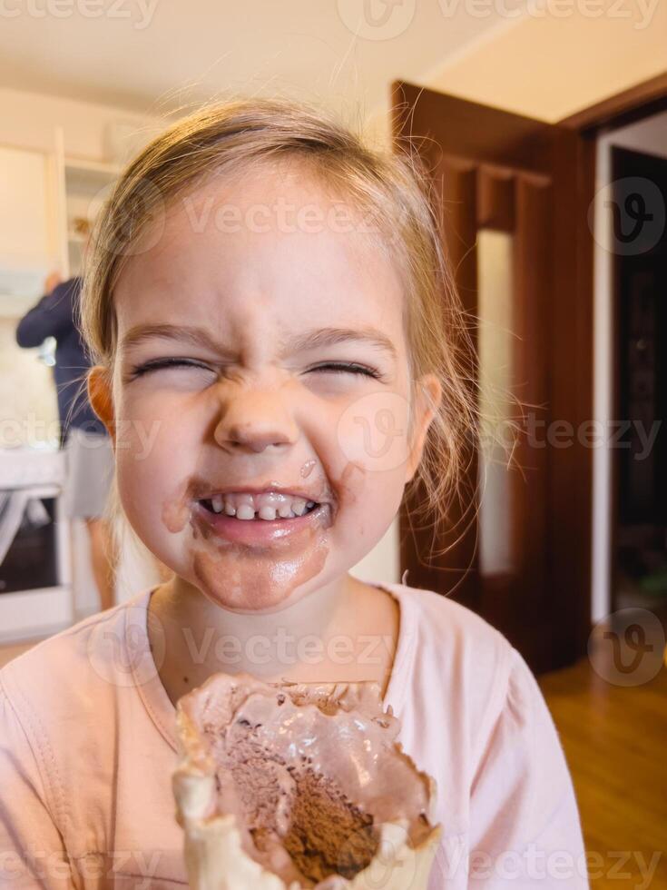 wenig lächelnd Mädchen mit ein schmutzig Gesicht hält Schokolade Eis Sahne im ein Waffel Tasse foto