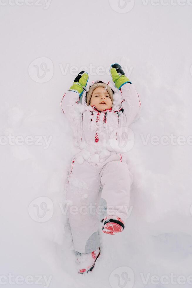 wenig Mädchen Lügen im ein Schneeverwehung Herstellung ein Schnee Engel mit ihr Augen geschlossen foto