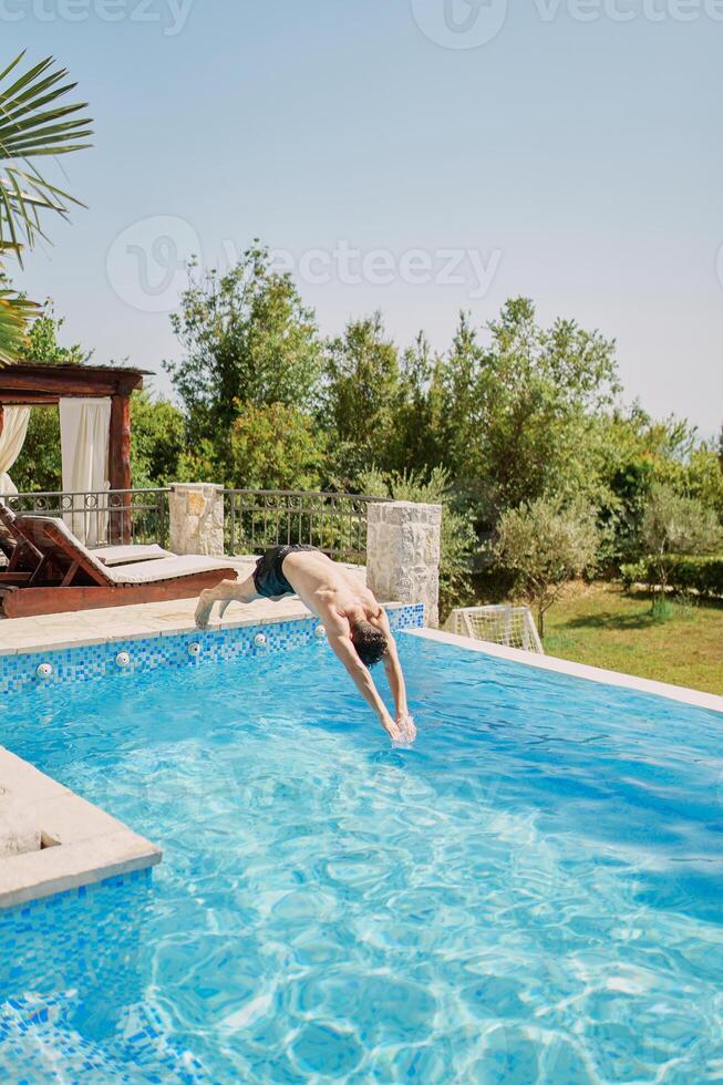jung Mann Tauchgänge mit seine Waffen nach vorne in das Schwimmbad in der Nähe von das Sonne Liegen foto