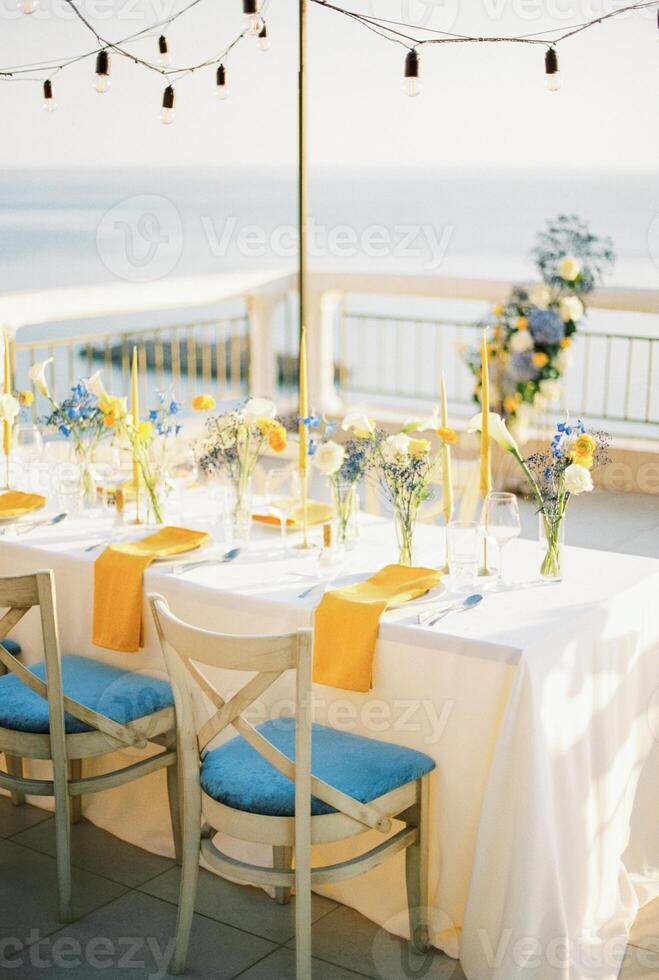 festlich Tabelle mit hängend Girlanden von Licht Glühbirnen steht auf das Terrasse über das Meer foto