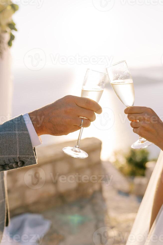 Braut und Bräutigam Klirren Brille von Champagner gegen das Hintergrund von ein sonnig Himmel. abgeschnitten. gesichtslos foto