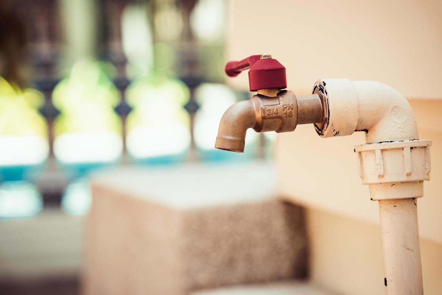 Wasserhahn mit Vintage rotem Wasserventil, Wasserleitung weiß lackiert, passend zur Wand, unscharfer Hintergrund. foto