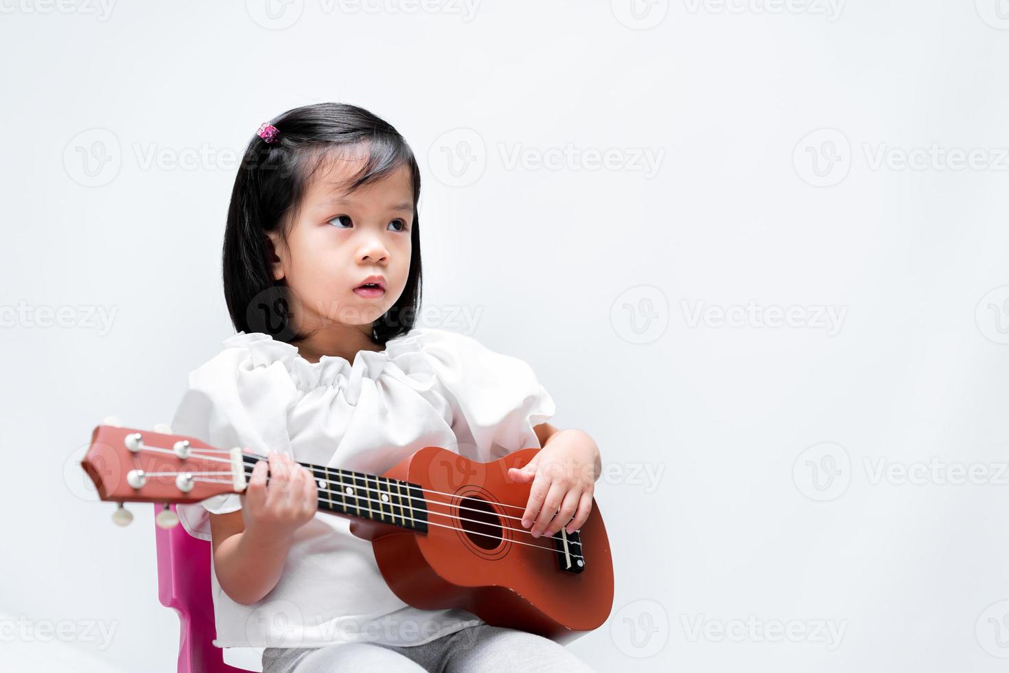 Schönes asiatisches Mädchen, das Ukulele-Musik auf isoliertem weißem Hintergrund im Studio spielt und lernt. foto