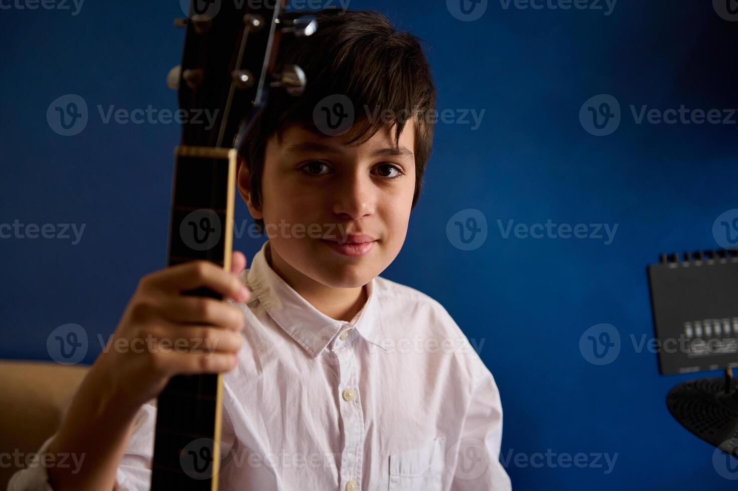 authentisch Porträt von ein Teenager Junge Gitarrist, jung talentiert Musiker halten akustisch Gitarre, suchen beim Kamera im das modern Musik- Studio. Personen. Musik- Lektion. Kinder Bildung und Unterhaltung foto