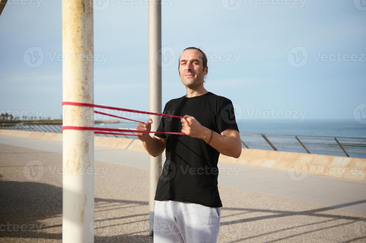 jung sportlich Mann Arbeiten aus auf Promenade, tun Schulter Drücken Sie mit Widerstand Band. aktiv gesund Lebensstil. Sport foto