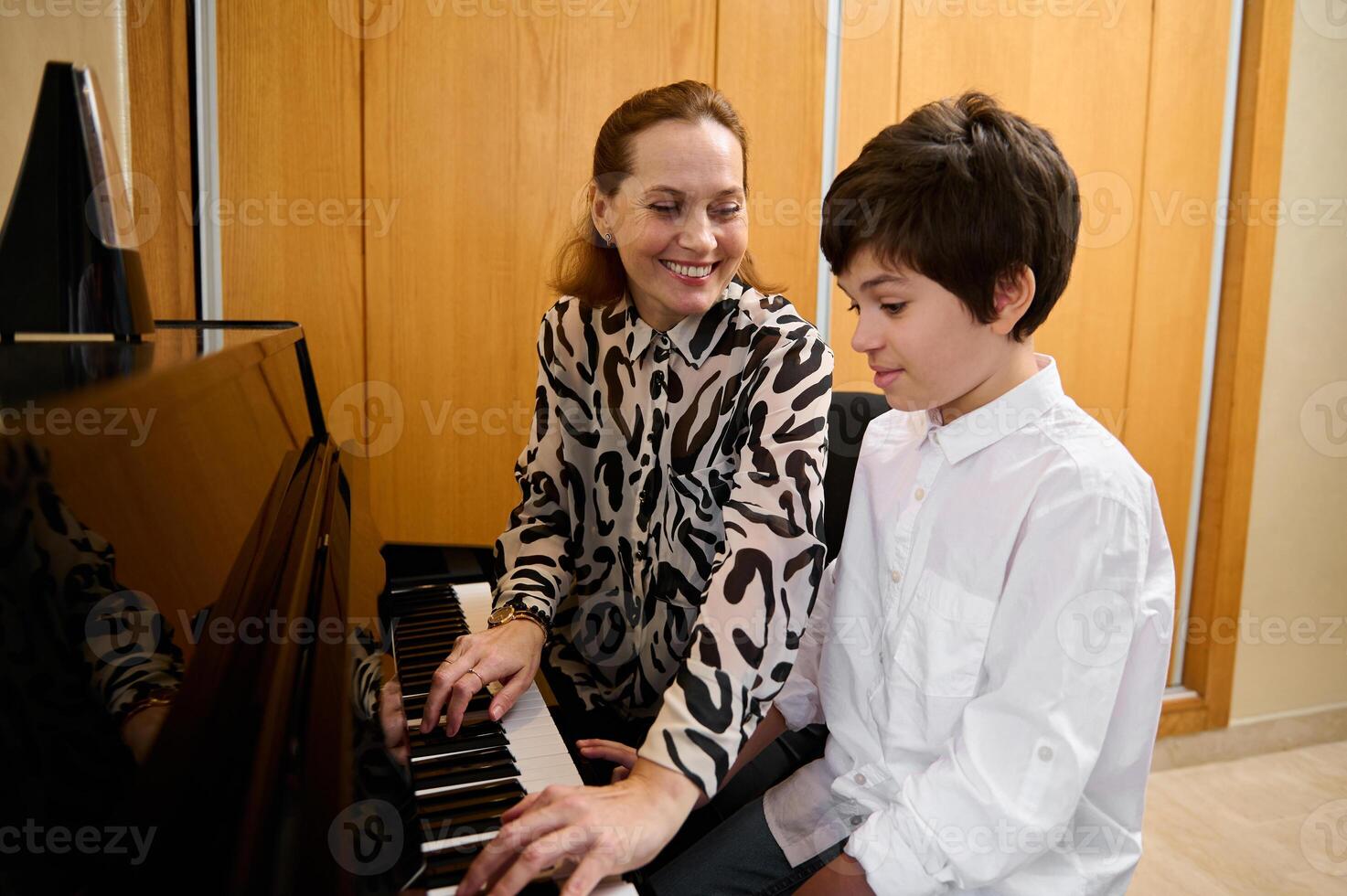 lächelnd liebend Mutter spielen Klavier, Sitzung in der Nähe von seine Jugendlicher Sohn, durchführen Weihnachten Sohn, genießen das Rhythmus von Melodie foto