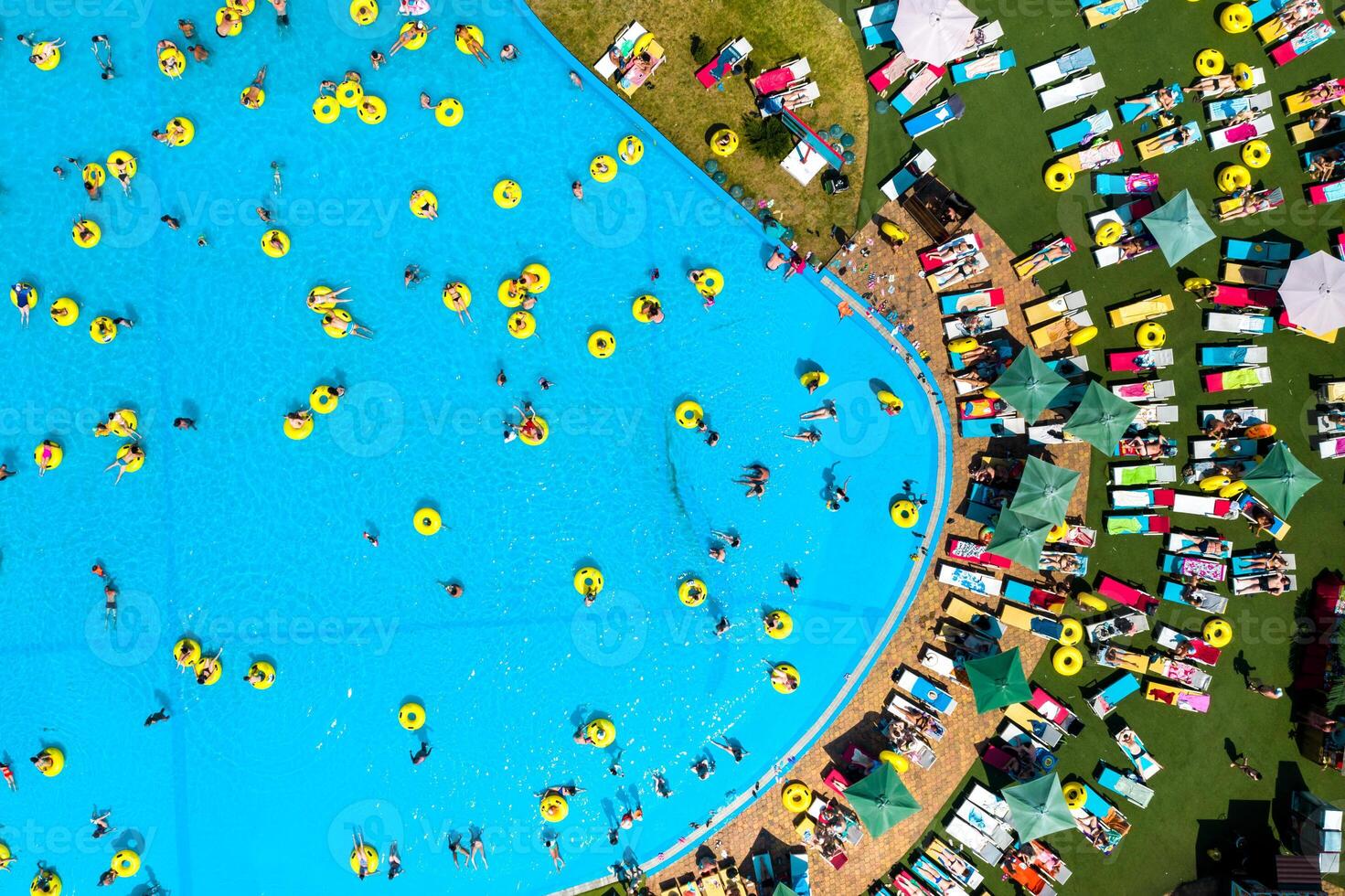 oben Aussicht von Menschen entspannend im das Schwimmbad auf Gelb aufblasbar Kreise und Sonne Betten auf das Strand foto