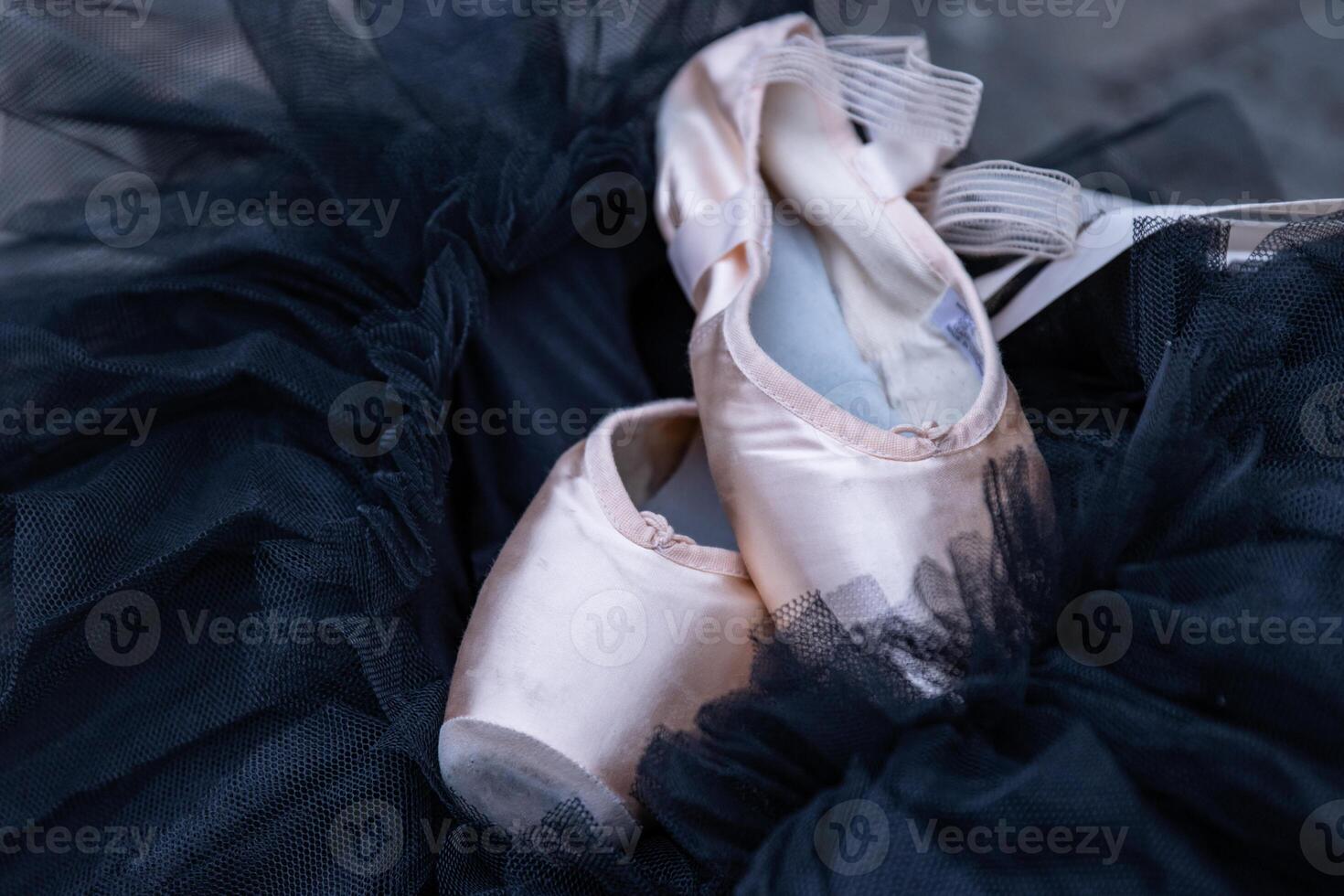 Nahansicht von das Rosa Ballett pointe Schuhe Verlegung auf das schwarz Chiffon Ballettröckchen. zwei Beige Ballett Hausschuhe auf das dunkel Hintergrund. minimalistisch Konzept. Kopieren Raum. selektiv Fokus. foto