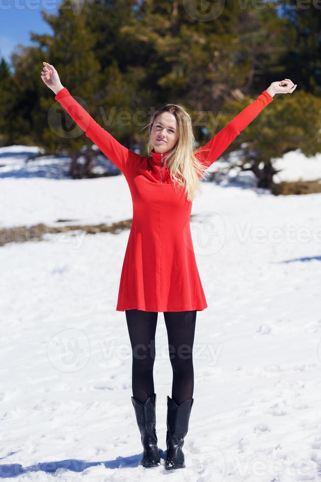 Frau trägt ein rotes Kleid und schwarze Strümpfe und öffnet ihre Arme vor Glück in den verschneiten Bergen. foto