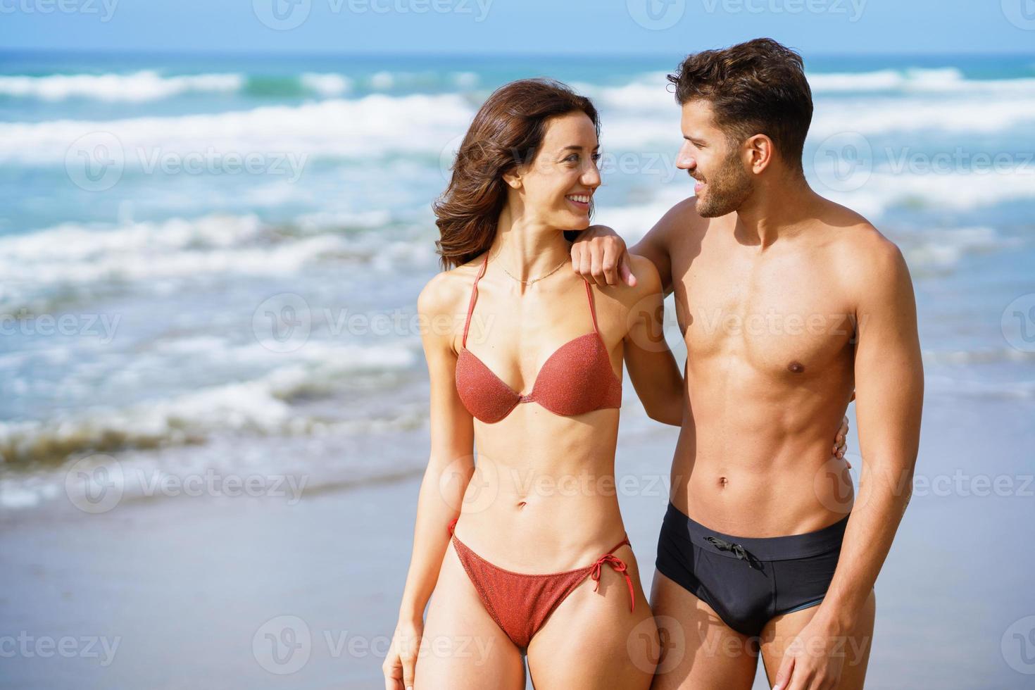 junges Paar schöner athletischer Körper, die zusammen am Strand spazieren gehen foto