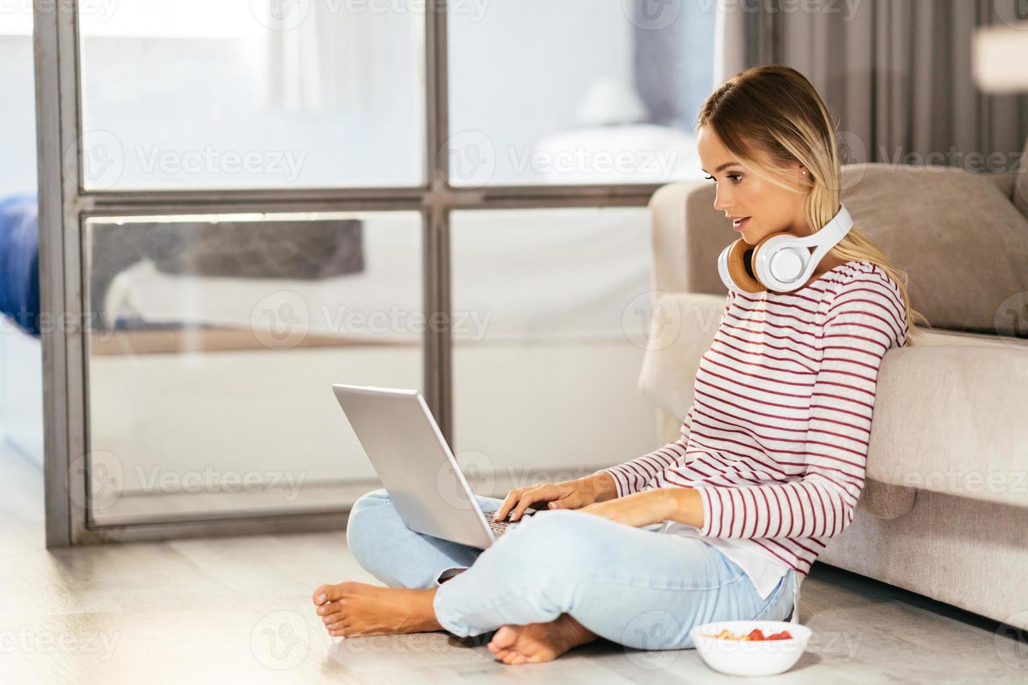 lächelnde junge Frau mit Kopfhörern und Laptop auf dem Sofa foto