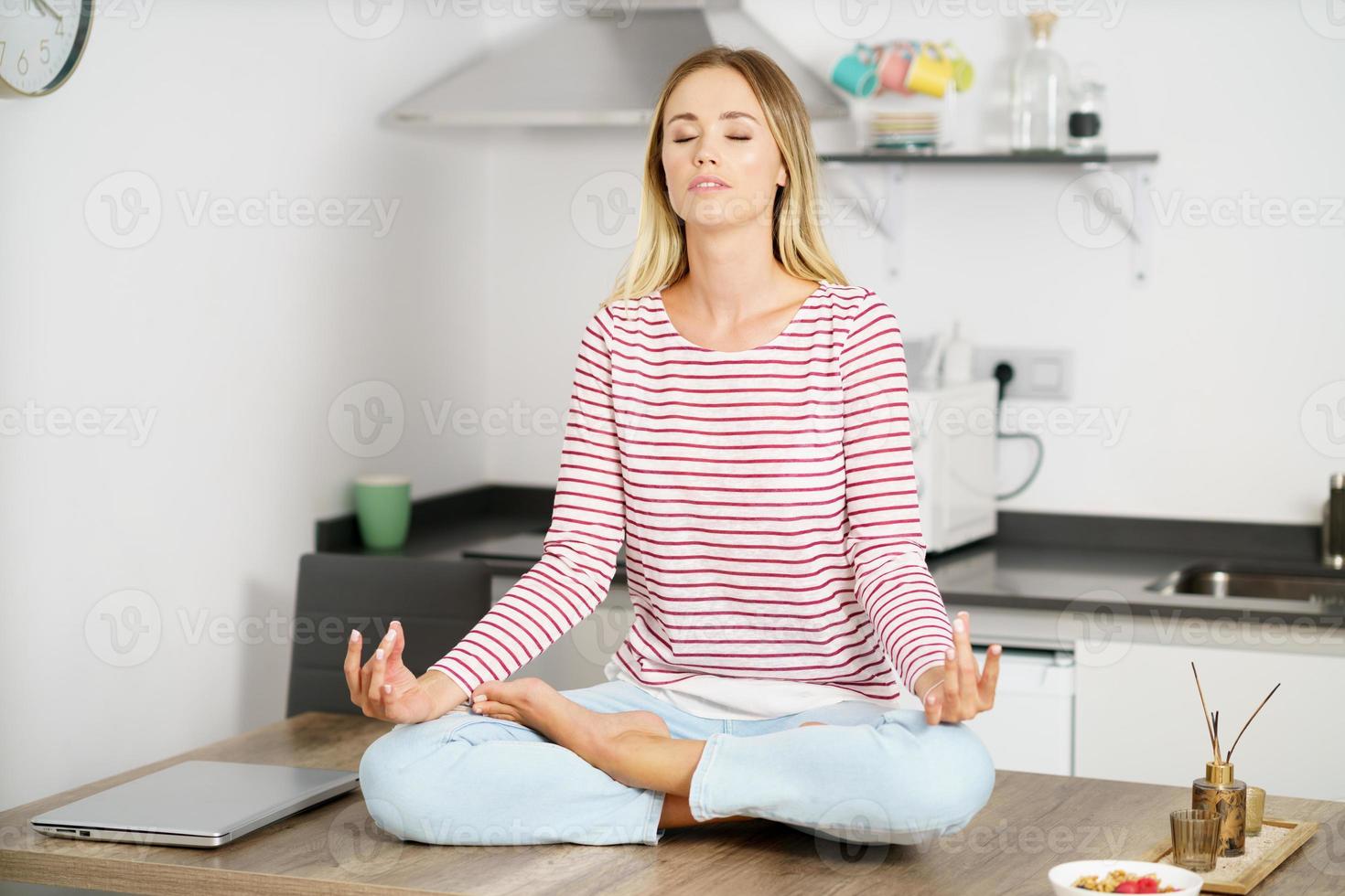 junge blonde Frau, die zu Hause in der Küche meditiert foto