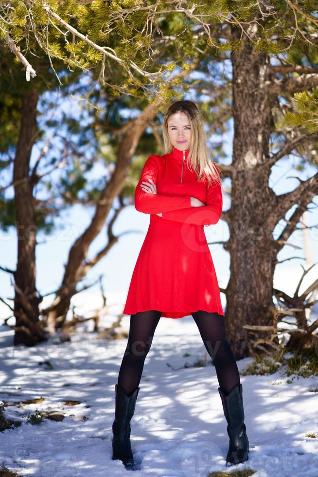 blonde Frau trägt ein rotes Kleid und schwarze Strümpfe in den verschneiten Bergen im Winter. foto