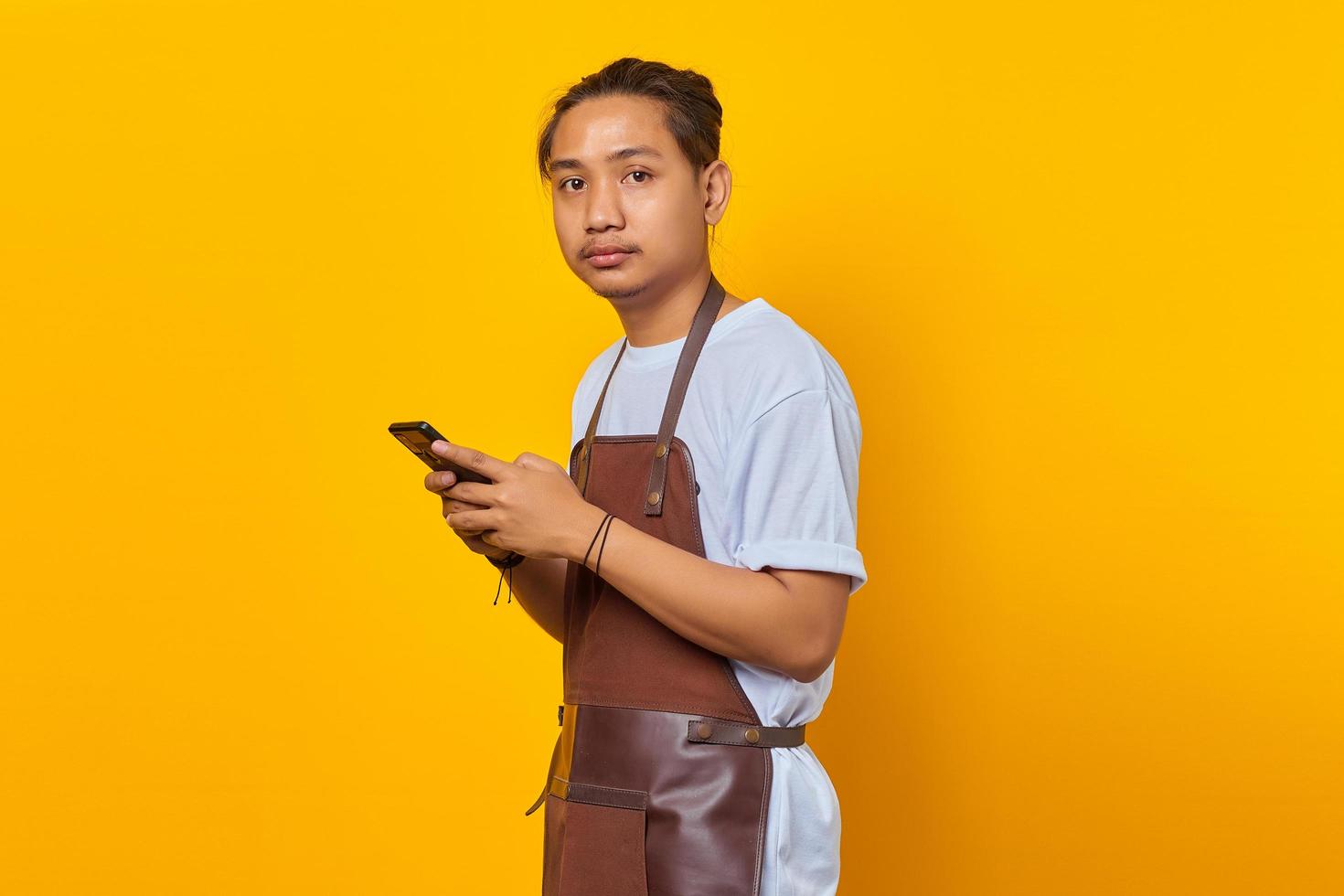 Porträt eines glücklichen asiatischen jungen Mannes mit Smartphone und Blick auf die Vorderseite auf gelbem Hintergrund foto