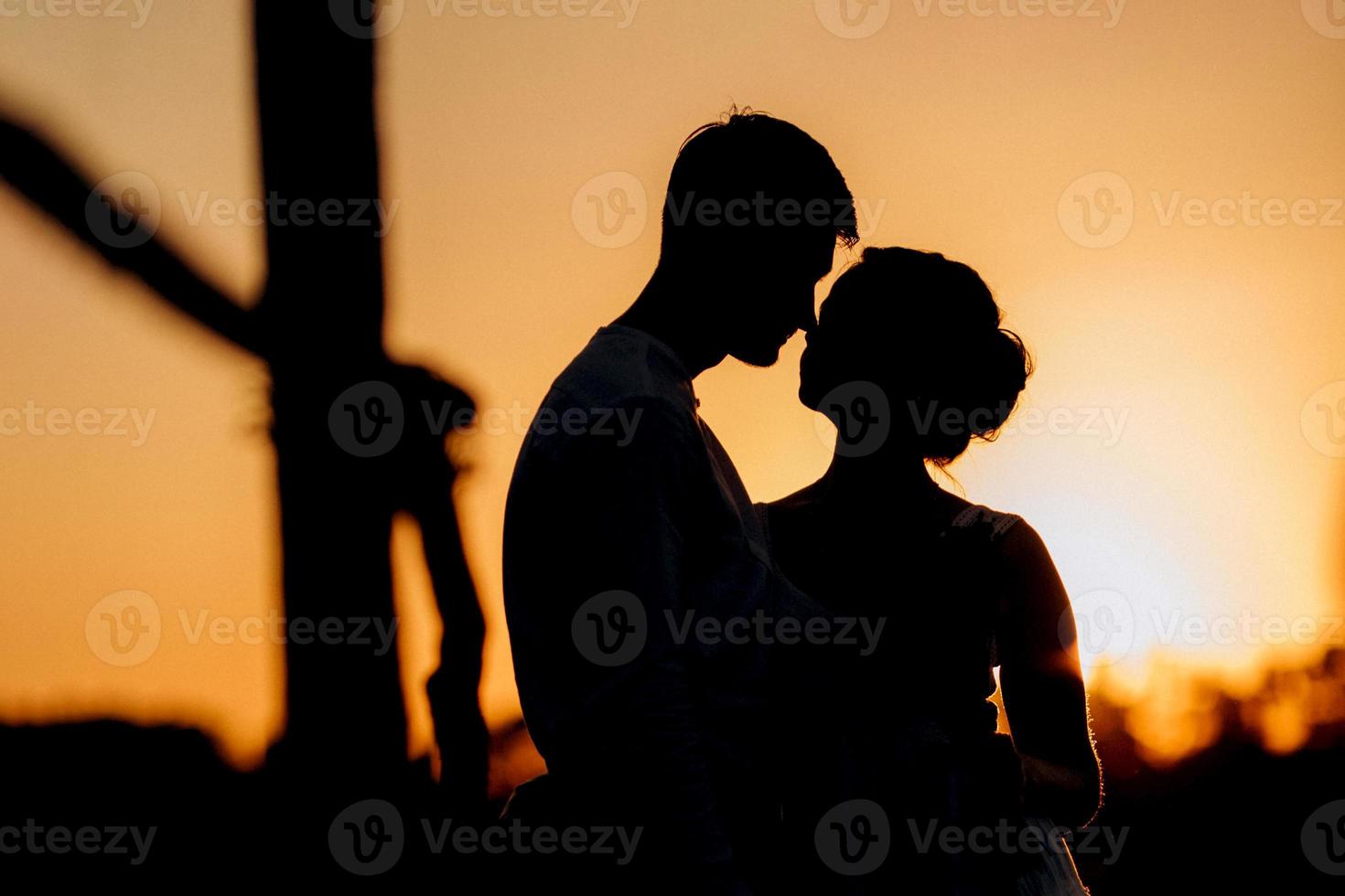 Mädchen in einem weißen Sommerkleid und ein Typ in einem weißen Hemd auf einem Spaziergang bei Sonnenuntergang mit einem Blumenstrauß foto