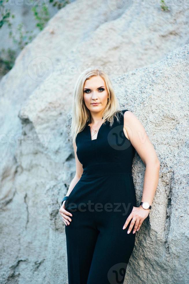 blondes Mädchen in einem schwarzen Hosenanzug mit blauen Augen auf dem Hintergrund eines Granitsteinbruchs foto