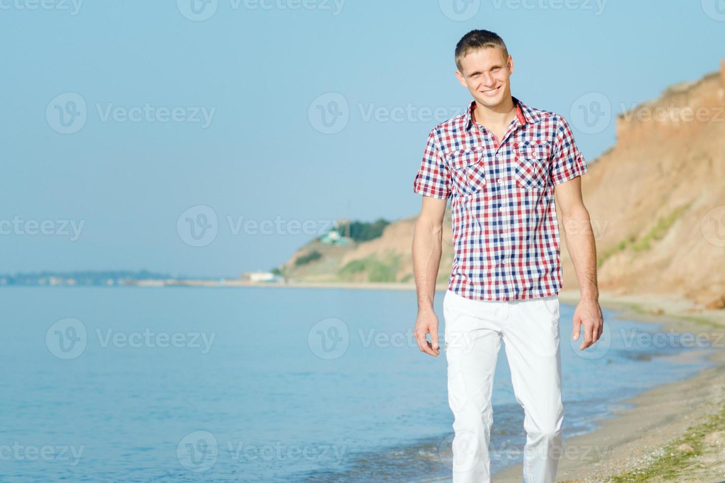 Kerl in weißen Hosen geht am Strand entlang gegen foto