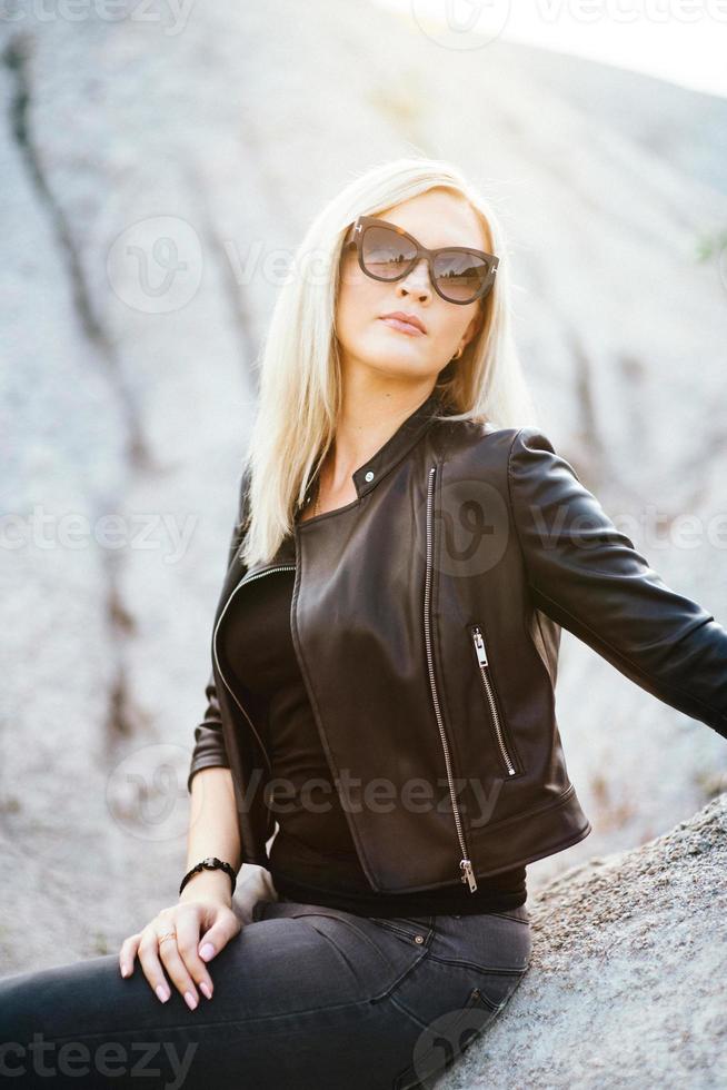 blondes Mädchen in einem schwarzen Hosenanzug mit blauen Augen auf dem Hintergrund eines Granitsteinbruchs foto