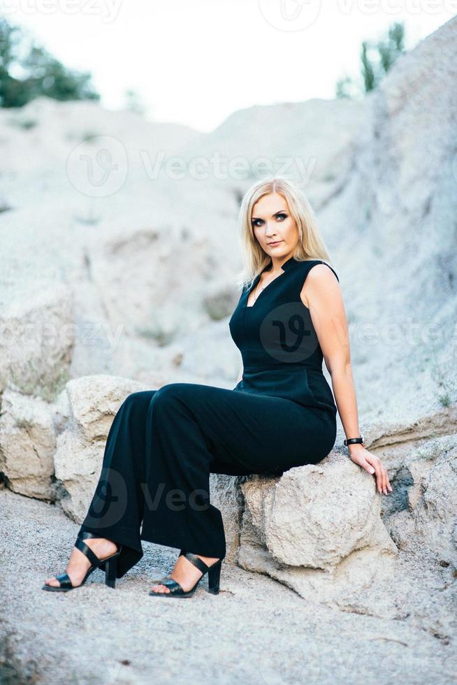 blondes Mädchen in einem schwarzen Hosenanzug mit blauen Augen auf dem Hintergrund eines Granitsteinbruchs foto